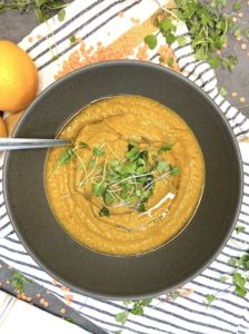 Presentation of red lentil soup bowl with a spoon and garnished with microgreens.