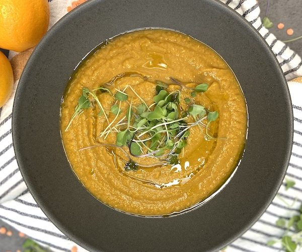 Presentation of red lentil soup bowl without a spoon and garnished with microgreens.