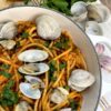 Part presentation of prepared bucatini alle vongole with clam shells next to garlic cloves parsley