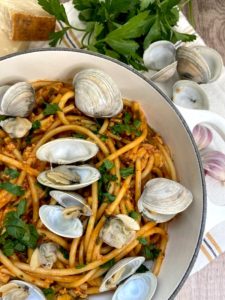 Part presentation of prepared bucatini alle vongole with clam shells next to garlic cloves parsley