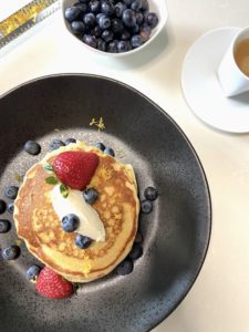 Pancakes next to blueberries bowl and espresso cup