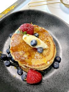 Pancakes with zest of lemon, berries and maple syrup on plate