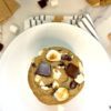Chocolate chip s'mores cookie on plate over dish towel next to glass of milk and marshmallows around