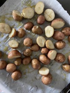 Single layer cooked baby potatoes on baking sheet lined with parchment paper and mixed with olive oil mixture