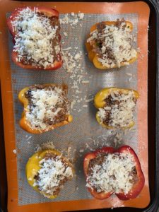 Baking tray lined with a silicone mat and with unbaked ground beef and quinoa stuffed bell pepper halves.