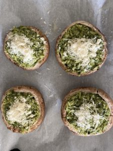 Four stuffed portobello mushrooms with pesto orzo topped with parmigiano reggiano on baking tray before going into the oven.