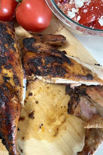 Grilled Spatchcock chicken on wood board with tomatoes