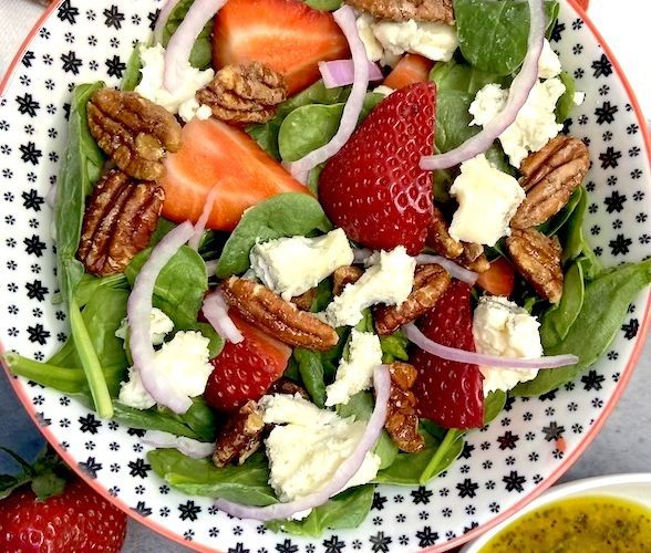 Close up picture of salad bowl with spinach, onions, pecans, strawberries and gorgonzola cheese