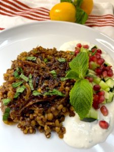Close up picture of dish presentation: braised lentils and bulgur with caramelized onions topped with mint and pomegranate seeds served with yoghurt sauce