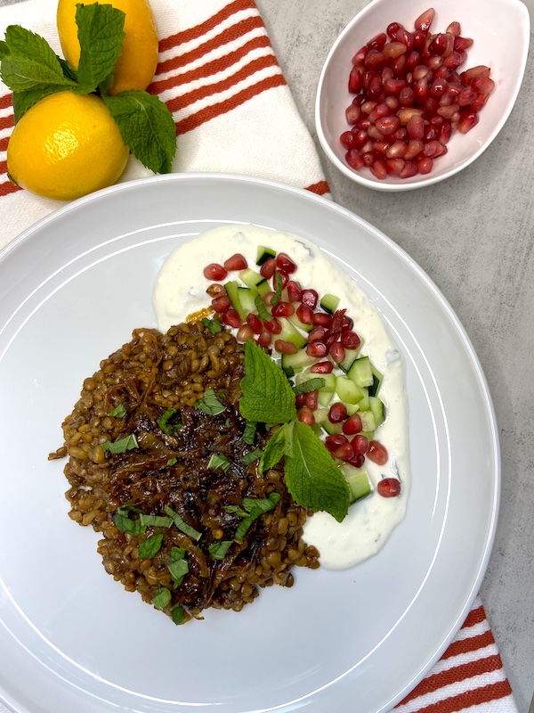 Syrian mujadara dish presentation with all the toppings on dish towel next to lemons and pomegranate seeds
