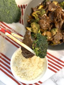 Chopsticks over rice with a piece of beef and brocoli.
