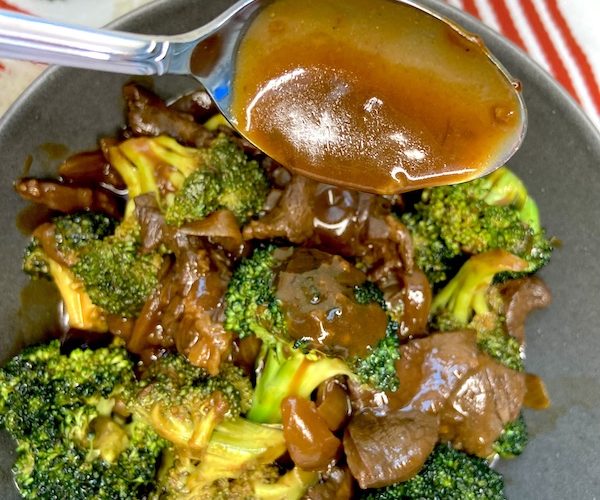 Close up picture of the beef and broccoli stir-fry with sauce dripping from spoon.