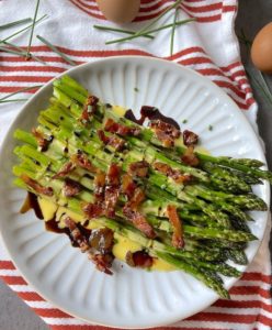 Plate of asparagus ready to be served, with sauce, drizzle of balsamic vinegar and topped with guanciale.