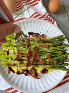 A fork dipping into the guanciale sautéed asparagus with sauce and a drizzle of balsamic vinegar.