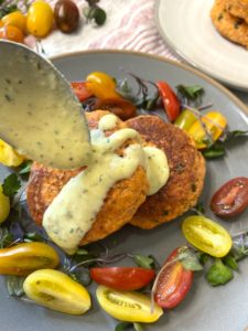 Spoonful of gribiche sauce pourring on salmon patties.