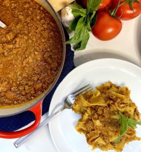 Picture showing a French oven with ragù sauce and next to it, a plate of fresh parpadelle