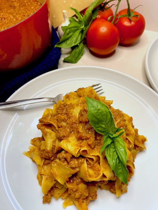 Plate of fresh parpardelle with veal and pork ragù sauce garnished with fresh basil