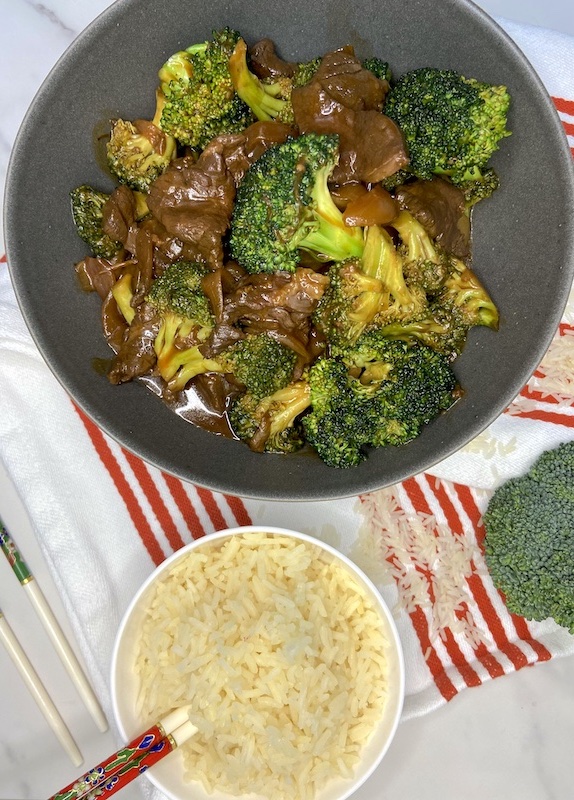 Presentation of stir-fry beef and brocoli in a bowl next to a small bowl of rice.