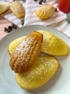 Four madeleines on plate dusted with some powdered sugar