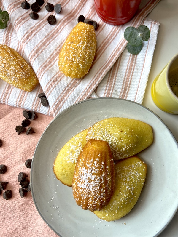 Four Madeleines dusted with powdered sugar on a plate.