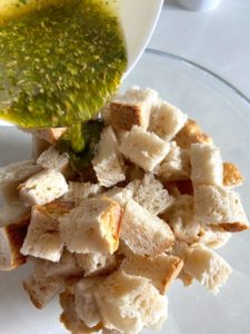 Pourring olive oil mixture into bread cubes.