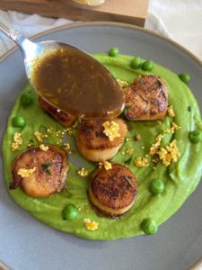 Picture showing a plate of seared scallops on pea puree with glazed butter and orange sauce poured on then.