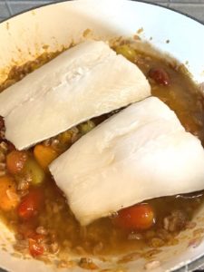 Adding two sea bass fish filets to poach, skin side down