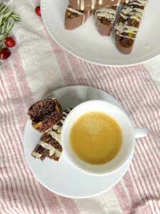 Chocolate Orange Pistachio Biscotti cut in half next to an espresso cup
