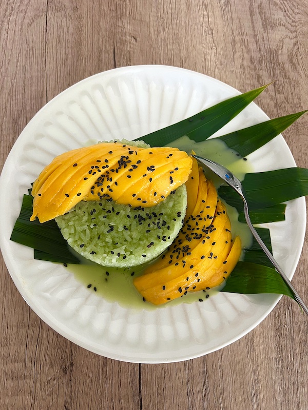 Plate of Pandan sticky rice with sliced mangoes with a spoon.